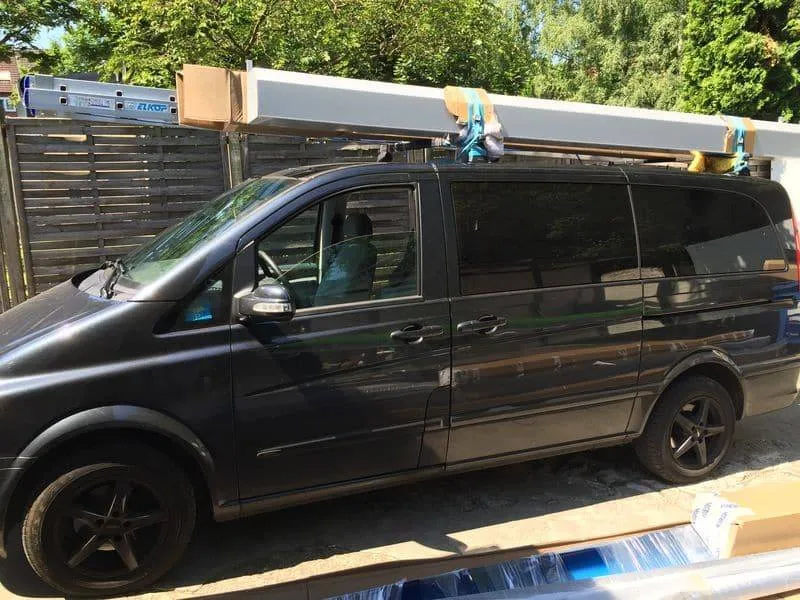 Schwarzer Lieferwagen parkte neben Baumaterialien, auf dessen Dach Gegenstände abgelegt waren.