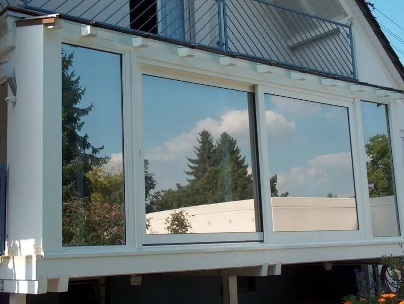 Große Fenster an einer modernen Hausfassade mit einer Spiegelung von Bäumen und Himmel.