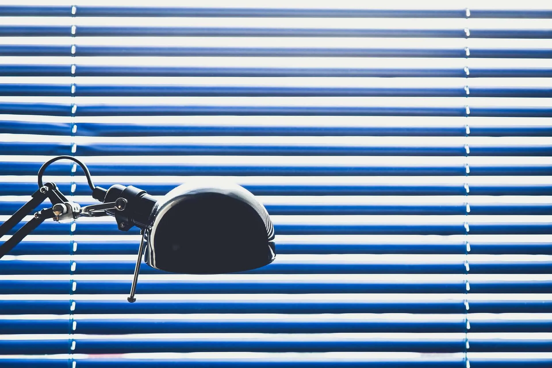 Eine Schreibtischlampe vor einem Hintergrund aus horizontalen Jalousien.