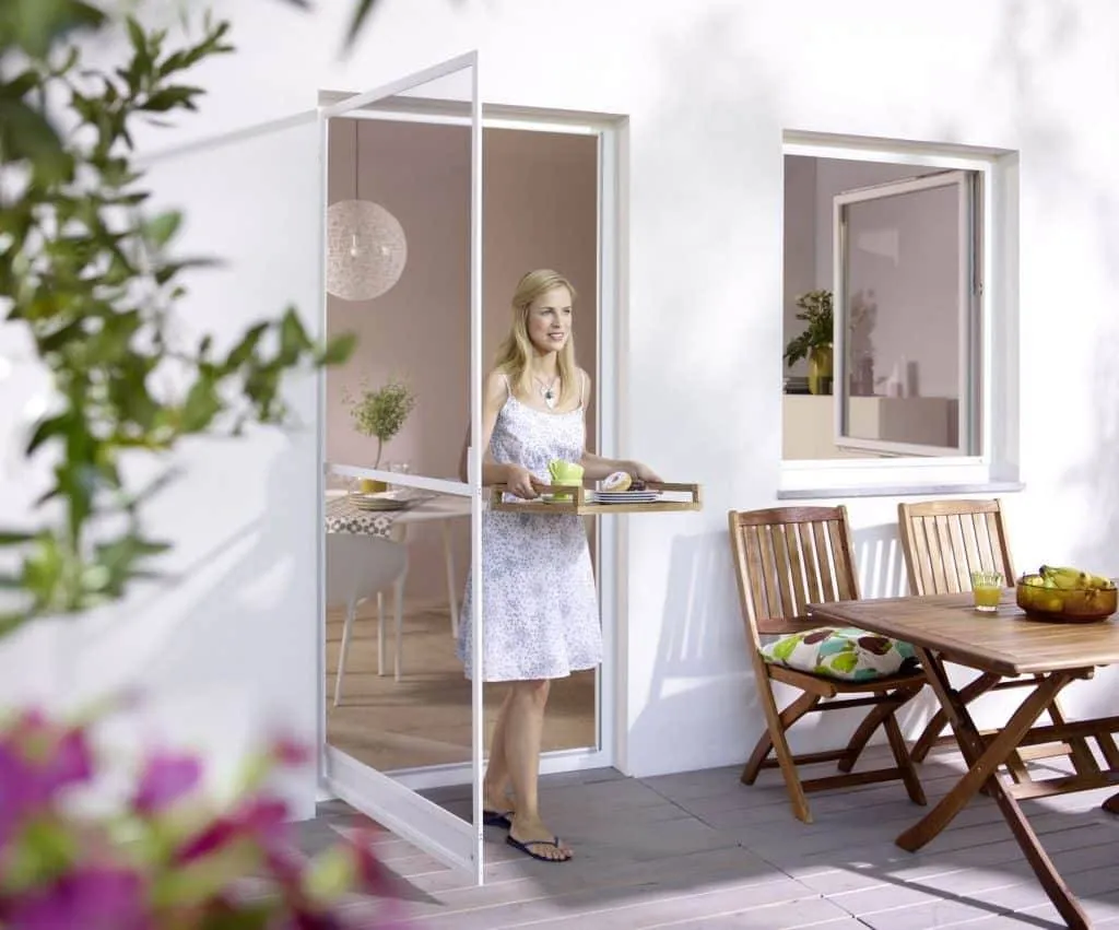 Eine Frau betritt eine sonnige Terrasse und trägt ein Tablett mit Erfrischungen.